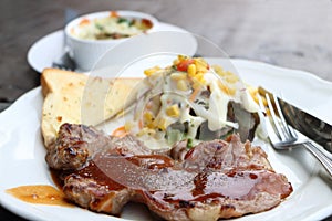 pork steak with sauce and salad vegetables with cream sauce and garlic bread grill in white round plate