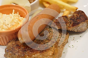 Pork steak with sausage and salad and french fries on dish