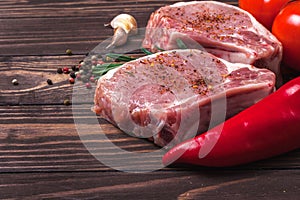 Pork steak with spices and rosemary. Juicy and fresh raw meat with vegetables and peas peas on a wooden tabletop