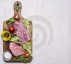 Pork steak with vegetables and herbs, meat knife and fork, on a cutting board oil and seasonings border ,place for text on