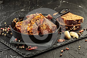 Pork stew in frying pan on black background, close up view