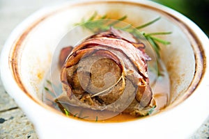 Pork tenderloin with bacon in white pan.