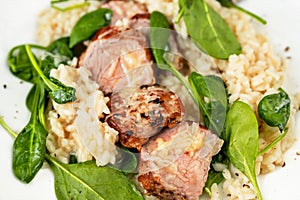 Pork tenderloin medallions on risotto with parmesan and spinach leaf,closeup