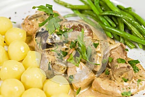 Pork tenderloin with potatoes and wild mushroom sauce and green beans on white plate