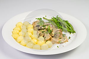 Pork tenderloin with potatoes and wild mushroom sauce and green beans on white plate