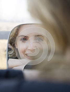 Porrtrait of smiling blonde woman in car side mirror