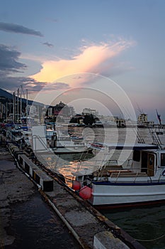 A port in a big city with fishing boats and a pier. Sunset and beautiful clouds.