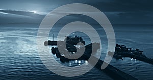 Port on blue moon light night background aerial view. Fishing boats near ocean pier silhouette.