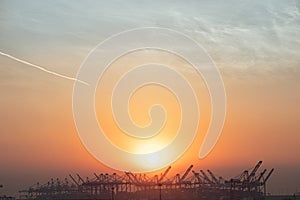 Port Cargo cranes silhouette at a beautiful sunrise, perfect industrial logistics background with negative space