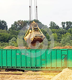 The port crane makes loading of wood chips into the freight wagons of the train, close-up, ladle, grab