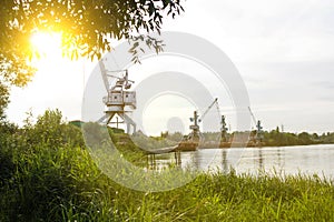 Port cranes with a bucket on the river bank, extraction of river sand, the sun