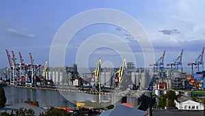 Port landscape with moving cargo loaders and grain elevators under blue sky