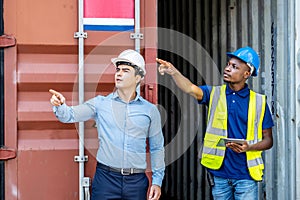 Port manager and a colleague tracking inventory while standing point to position loading Containers box from Cargo freight ship at