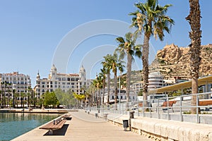 Port side embankment in Alicante, Spain. Sidewalk near marina, palm trees, historical buildings on background