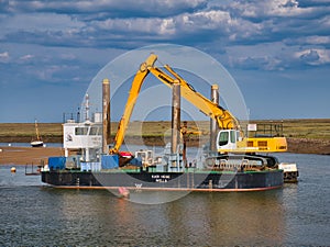 In the Port of Wells, Norfolk, UK, harbour dredger Kari Hege, a specialist 20m by 10m spud-leg pontoon with depth monitoring