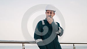Port worker talking on walkie-talkie radio while doing cargo logistics control in seaport