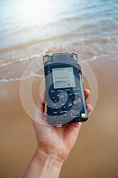 Portable audio recorder in hand recording ambient sounds of sea