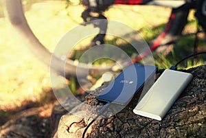 A portable charger charges the smartphone. Power Bank with cable against the background of wood and bicycle