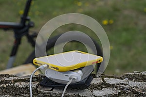 A portable charger charges the smartphone. Power Bank with cable against the background of wood and bicycle