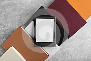 Portable e-book reader on hardcover books on grey textured table, flat lay