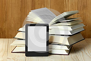 Portable e-book reader and open hardcover books on wooden table