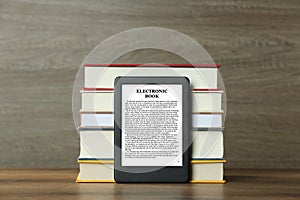 Portable e-book reader and stack of hardcover books on wooden table