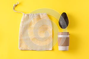 Portable eco cup, produce bag, avocado on yellow surface. Coffee mug, bag for grocery shopping, vegetable. Flat lay, top view,
