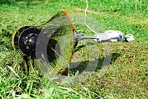 Portable electric grass trimmer lying on green lawn