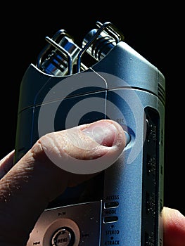 Portable field recorder with stereo XY microphones held in hand prepared to press record button