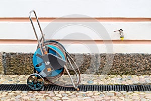 A portable garden hose in a blue reel with wheels for watering lawn, flowers and other plants.
