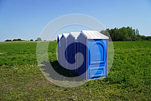 Portable plastic toilets in the field on the grass on a background of blue sky