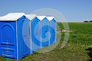 Portable plastic toilets in the field on the grass on a background of blue sky