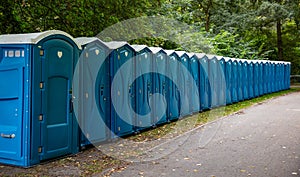 Portable WC cabins in the park. A line of chemical toilets for a festival, against a forest