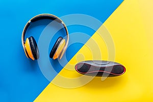 Portable wireless speakers and headphones as gadgets for listen to the music on blue and yellow background top view