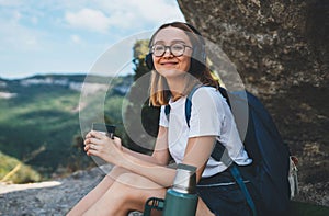 Portait fun tourist girl in glasses leisure after walking on mountains and drinking tea or coffee outdoor,  active female traveler