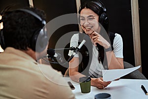 Portait of happy female radio host smiling, listening to male guest, presenter and holding a script paper while