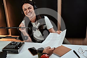 Portait of happy female radio host smiling, receiving a script paper from her male colleague while moderating a live