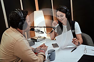 Portait of happy female radio host smiling, talking to male guest, presenter while moderating a live show in studio