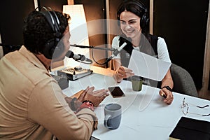 Portait of happy female radio host smiling, talking to male guest, presenter while moderating a live show in studio