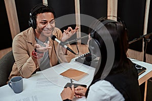 Portait of happy male radio host smiling, talking to female guest while moderating a live show in studio