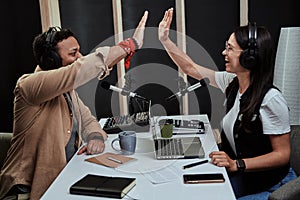 Portait of two cheerful radio hosts, young man and woman giving high five while talking, moderating a live show in