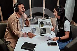 Portait of two cheerful radio hosts, young man and woman laughing while discussing various topics, reading a script