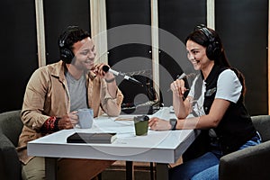 Portait of two happy radio hosts, man and woman smiling while talking with each other, moderating a live show in studio