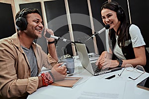 Portait of two happy radio hosts, young man and woman talking with each other while moderating a live show in studio