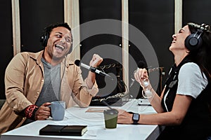 Portait of two radio hosts, man and woman laughing while talking with each other, moderating a live show in studio