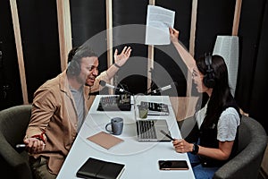 Portait of two radio hosts, young man and woman looking emotional while talking with each other, moderating a live show