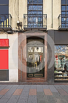 Portal of a building with a narrow door painted in black and golden brass details and a reddish facade at ground level