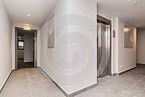 Portal of a house with white walls, gray floors and elevator with metal doors in stainless steel