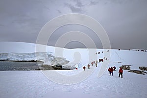 There is the sea next to the thick ice sheet. Tourists are walking on the thick ice field.