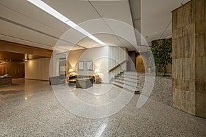 Portal of a residential house with stairs and granite floors, papered walls and an elevator with a brown metal door and a lounge